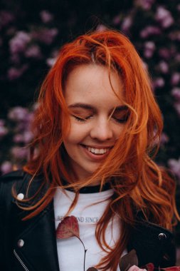 Parkta çiçek açan ağaca poz veren güzel kızıl saçlı kız.