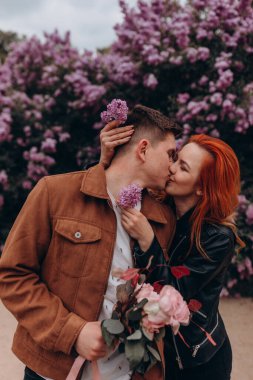 Mutlu çift arka planda çiçeklerle poz veriyor. 