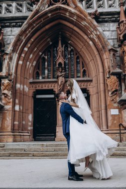 Mutlu genç damat düğün günü kilisenin yanında çekici gelini kucaklıyor ve taşıyor.          