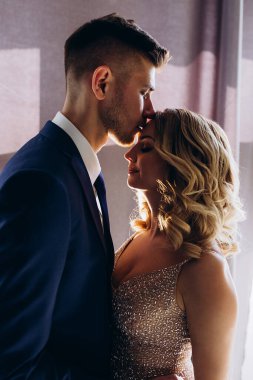 Şık giyinmiş güzel bir gelin ve yatak odasında poz veren yakışıklı bir damat.