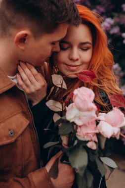 Parkta çiçek açan ağaçlarla sarılıp öpüşen genç bir çift. 