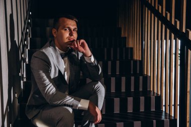 Çatı katında oturan takım elbiseli ve papyonlu yakışıklı genç damat.