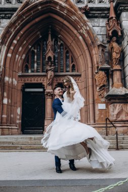 Mutlu genç damat düğün günü kilisenin yanında çekici gelini kucaklıyor ve taşıyor.          