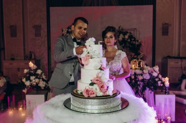 Mutlu gelin ve damat düğün gününü kutluyor ve düğün pastasını kesiyor.           