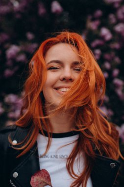 Parkta çiçek açan ağaca poz veren güzel kızıl saçlı kız.