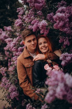 Mutlu çift arka planda çiçeklerle poz veriyor. 