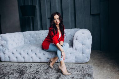 Genç, güzel, esmer, kırmızı ceketli kadın kanepede oturuyor. 