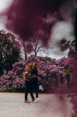 Genç ve güzel bir çift çiçek açan çalılara karşı poz veriyor. 