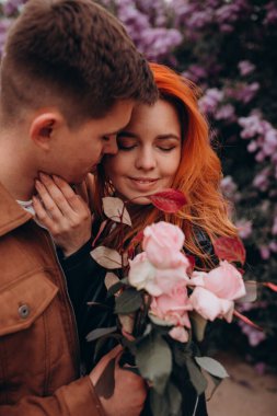 Parkta çiçek açan ağaçlarla sarılıp öpüşen genç bir çift. 
