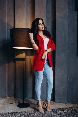 Kırmızı ceketli güzel, genç esmer kadın lambanın yanında poz veriyor. 