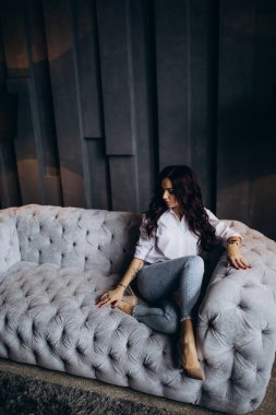 Stüdyoda gri koltukta poz veren güzel esmer kadın.