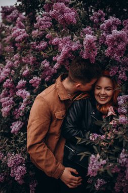 Mutlu çift arka planda çiçeklerle poz veriyor. 