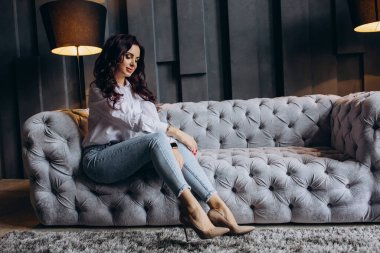 Stüdyoda gri koltukta poz veren güzel esmer kadın.