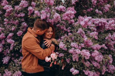 Genç ve güzel bir çift çiçek açan çalılara karşı poz veriyor. 