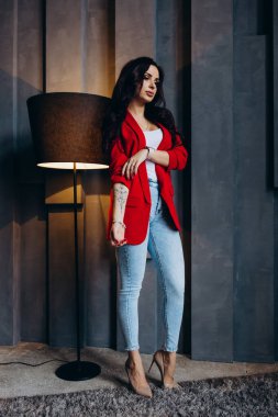 Kırmızı ceketli güzel, genç esmer kadın lambanın yanında poz veriyor. 