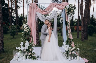 Düğün kemerinin yanında poz veren mutlu gelin ve damat parktaki düğün töreninde            