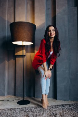 Kırmızı ceketli güzel, genç esmer kadın lambanın yanında poz veriyor. 