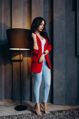 Kırmızı ceketli güzel, genç esmer kadın lambanın yanında poz veriyor. 