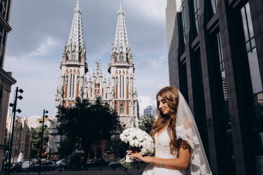 Gelinlik giymiş çekici genç gelin elinde bir buket çiçekle şehirde       