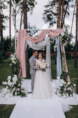 Düğün kemerinin yanında poz veren mutlu gelin ve damat parktaki düğün töreninde            