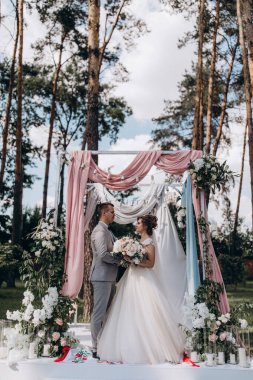 Düğün kemerinin yanında poz veren mutlu gelin ve damat parktaki düğün töreninde            