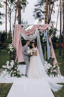 Düğün kemerinin yanında poz veren mutlu gelin ve damat parktaki düğün töreninde            