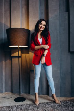 Kırmızı ceketli güzel, genç esmer kadın lambanın yanında poz veriyor. 