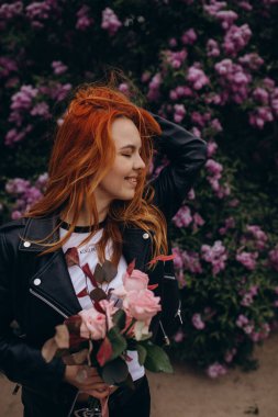 Parkta çiçek açan ağaca poz veren güzel kızıl saçlı kız.