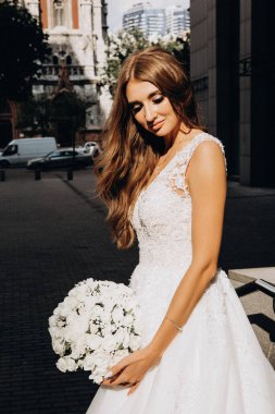Gelinlik giymiş çekici genç gelin elinde bir buket çiçekle şehirde       
