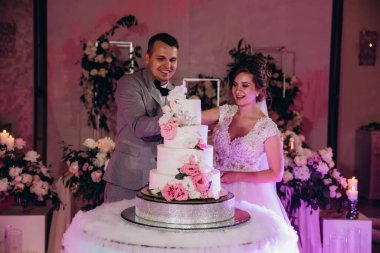 Mutlu gelin ve damat düğün gününü kutluyor ve düğün pastasını kesiyor.           