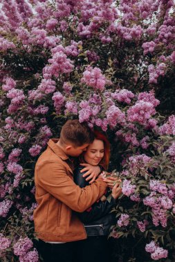 Mutlu çift arka planda çiçeklerle poz veriyor. 