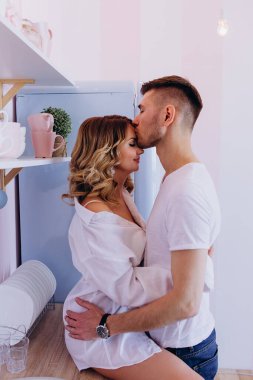 Mutlu genç çiftin sabah mutfakta sarılıp öpüşmelerinin yan görüntüsü.