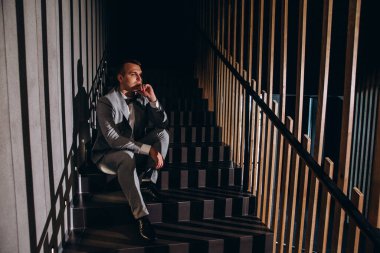 Modern binanın merdivenlerinde oturan takım elbiseli genç şık bir adam.