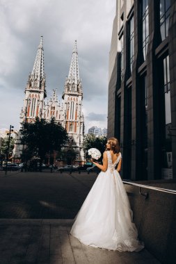 Gelinlik giymiş çekici genç gelin elinde bir buket çiçekle şehirde       