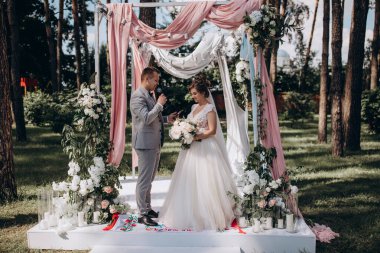 Düğün kemerinin yanında poz veren mutlu gelin ve damat parktaki düğün töreninde            