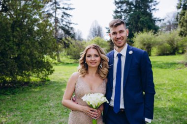 Mutlu genç gelin ve damat parkta kameraya gülümsüyor.