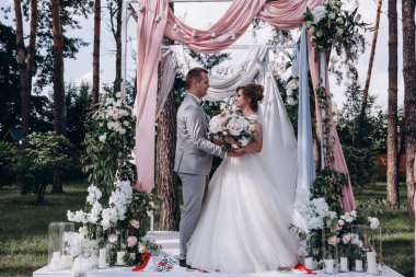 Düğün kemerinin yanında poz veren mutlu gelin ve damat parktaki düğün töreninde            