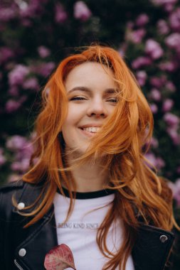 Parkta çiçek açan ağaca poz veren güzel kızıl saçlı kız.