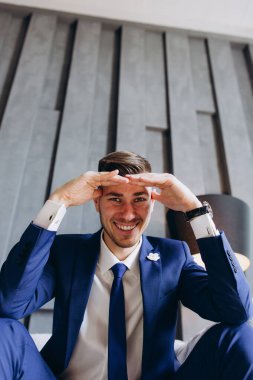 Şık takım elbiseli yakışıklı genç adamın portresi oturuyor ve kameraya gülümsüyor.