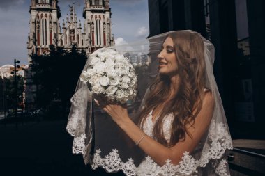 Gelinlik giymiş çekici genç gelin elinde bir buket çiçekle şehirde       