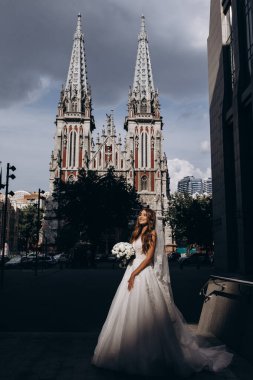 Gelinlik giymiş çekici genç gelin elinde bir buket çiçekle şehirde       