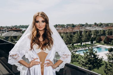 Beyaz iç çamaşırlı, ipek cüppeli ve terasta poz veren güzel bir gelin.       