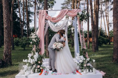Düğün kemerinin yanında poz veren mutlu gelin ve damat parktaki düğün töreninde            