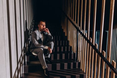 Takım elbiseli genç adamın portresi merdivenlerde oturuyor ve başka tarafa bakıyor. 