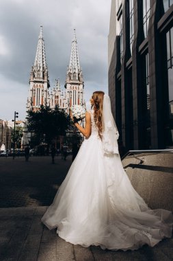 Gelinlik giymiş çekici genç gelin elinde bir buket çiçekle şehirde       