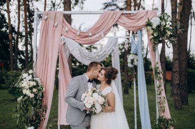 Düğün kemerinin yanında poz veren mutlu gelin ve damat parktaki düğün töreninde            