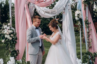 Düğün kemerinin yanında poz veren mutlu gelin ve damat parktaki düğün töreninde            