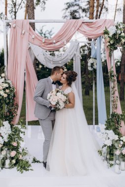 Düğün kemerinin yanında poz veren mutlu gelin ve damat parktaki düğün töreninde            