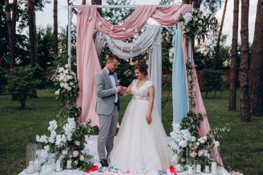 Düğün kemerinin yanında poz veren mutlu gelin ve damat parktaki düğün töreninde            