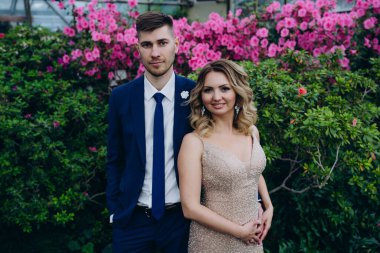 Mutlu gelin ve damat, botanik bahçesinde mor çiçeklerin önünde köprüde kucaklaşıyorlar. 